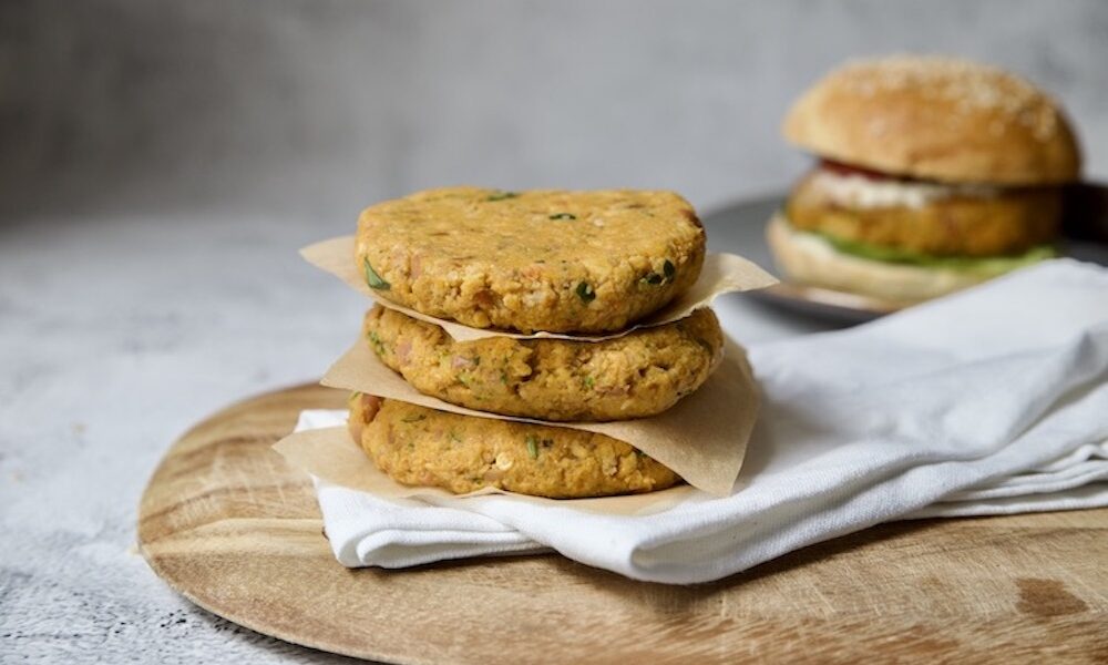 pila di hamburger vegetali ed un hamburger con panino nello sfondo