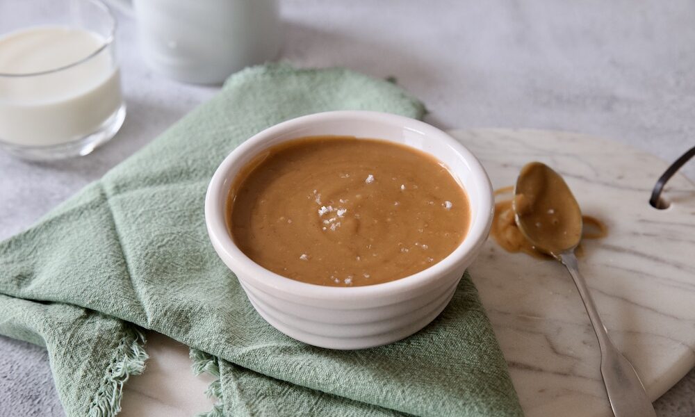 salsa al caramello salato in una ciotola, latte sullo sfondo