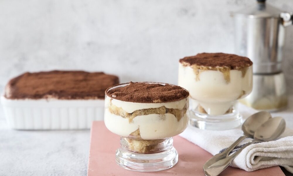 Tiramisù in coppette con cucchiaini e caffettiera nello sfondo