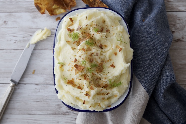 purè di patate in una ciotola ovale, guarnito con erbe e bucce di patate croccanti